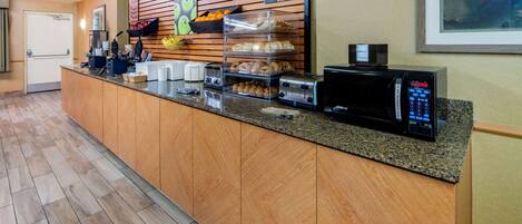 A hotel reception area with a counter, a microwave, a toaster, and a display case with pastries.