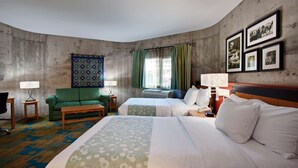 A hotel room with a large bed, two smaller beds, a green sofa, a patterned rug, a desk with a lamp, and a wall with framed pictures. - La Quinta Inn & Suites by Wyndham Irvine Spectrum (Irvine)