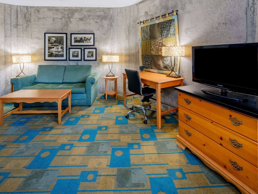 A room with a blue sofa, a wooden desk, a television, and a patterned carpet.