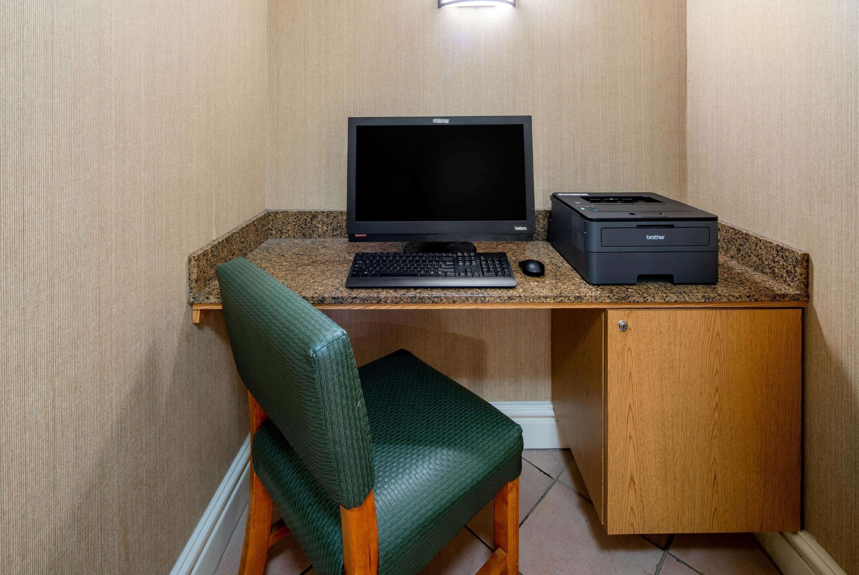 A small office space with a desktop computer, a printer, and a green chair.