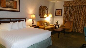A hotel room with a large bed, a sofa, a chair, a small table, and two lamps.