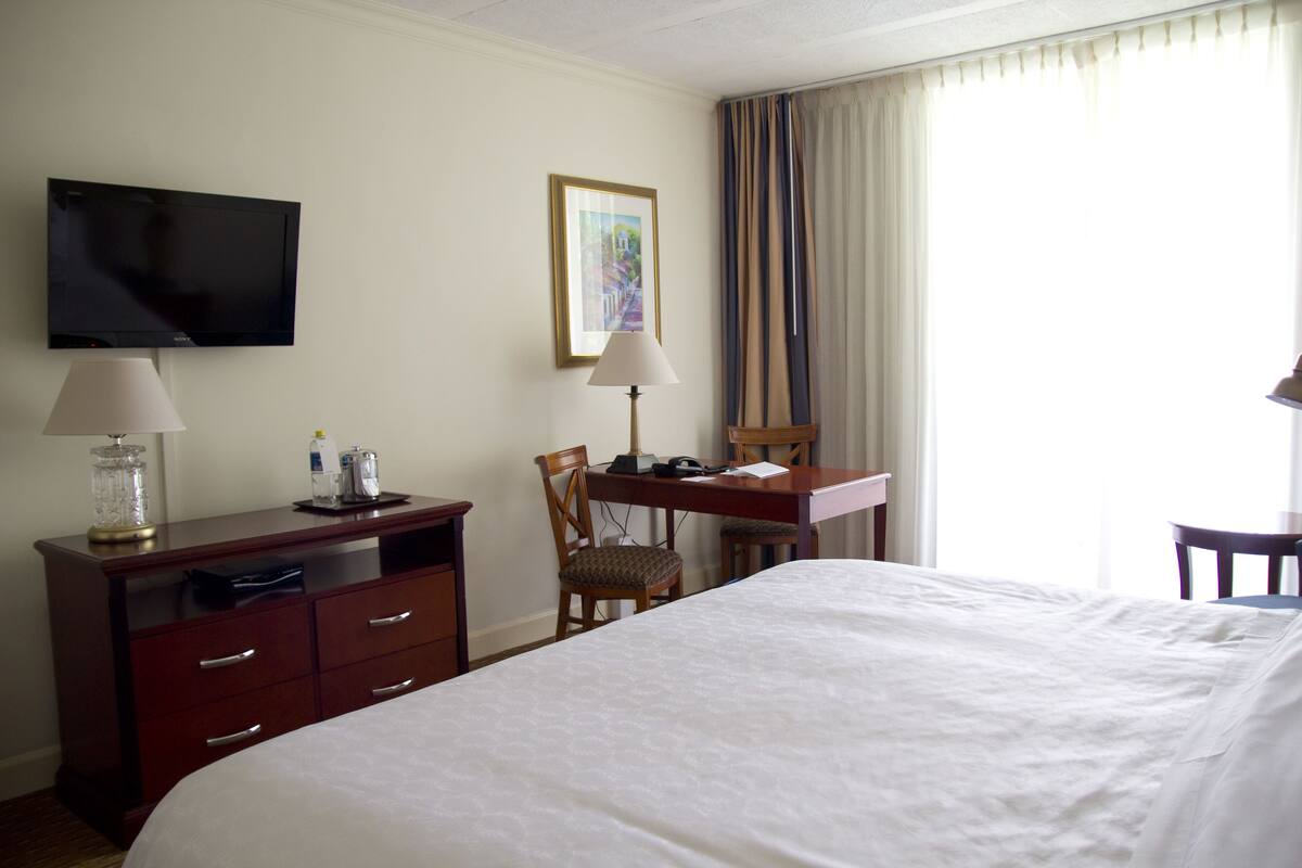 A hotel room with a bed, a desk, a chair, a television, and a lamp.