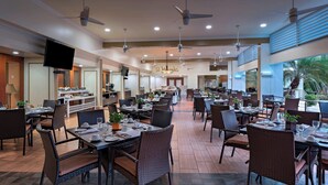 Un restaurante espacioso con varias mesas y sillas, ventiladores de techo y una pantalla de televisión.