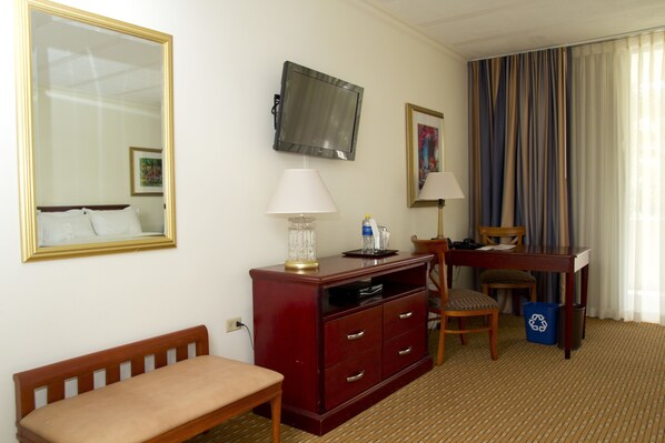 A hotel room with a bed, a desk, a TV, a lamp, a chair, and a waste bin.