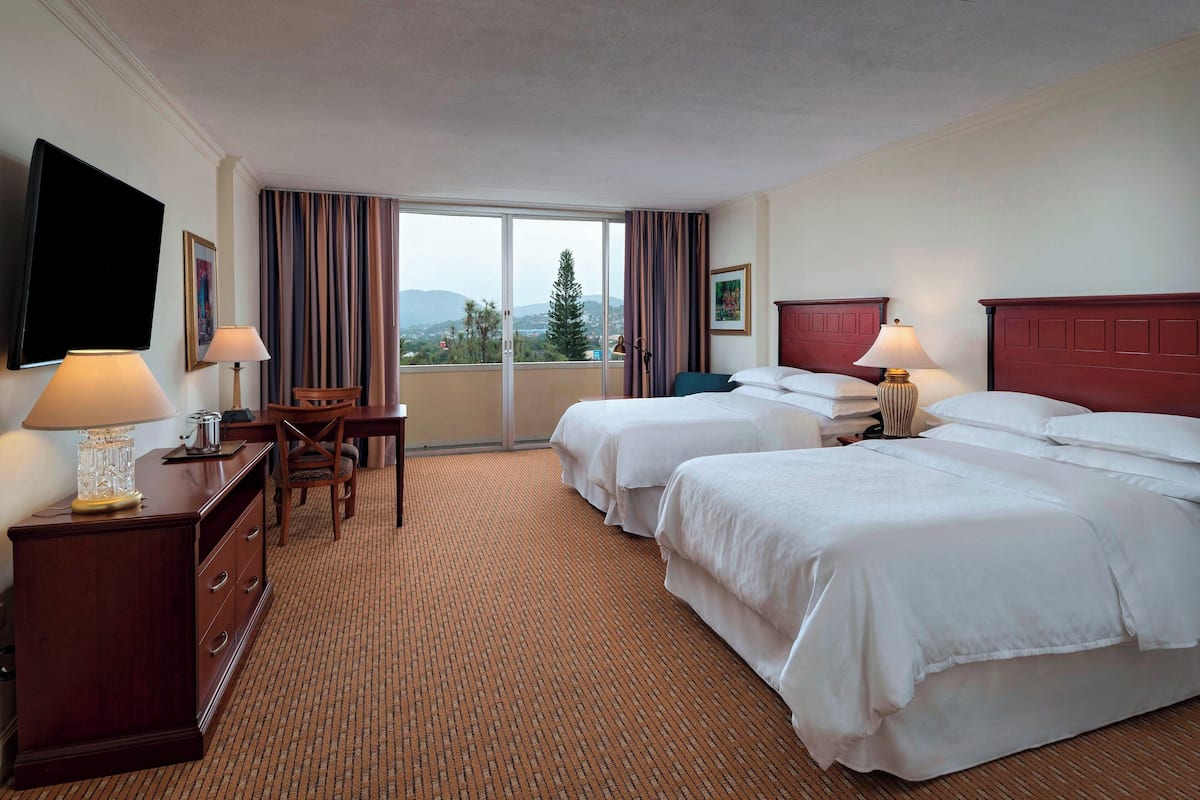 A hotel room with two beds, a desk, a chair, and a TV.