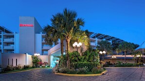 Un hotel Sheraton con diseño moderno, destacando un edificio con el letrero 'Sheraton', rodeado de exuberante vegetación y palmeras.