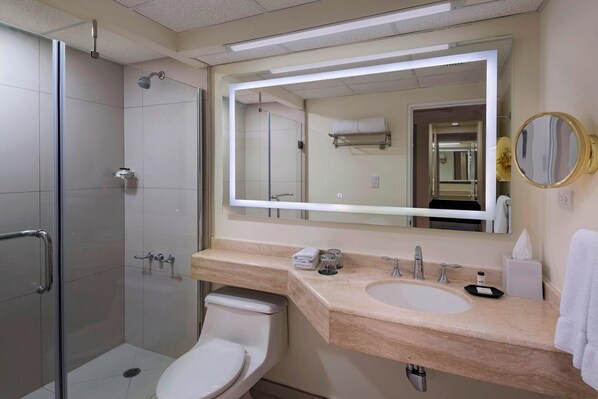 Un baño moderno con cabina de ducha de vidrio, inodoro blanco, lavabo con espejo y un perchero para toallas.