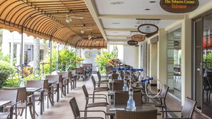 Un café al aire libre con mobiliario de mimbre, una zona de estar cubierta y un cartel que dice 'The Tobacco Corner Habanos'.