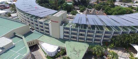 Un edificio de varios pisos con techo curvo, paneles solares y un estacionamiento con un auto amarillo.