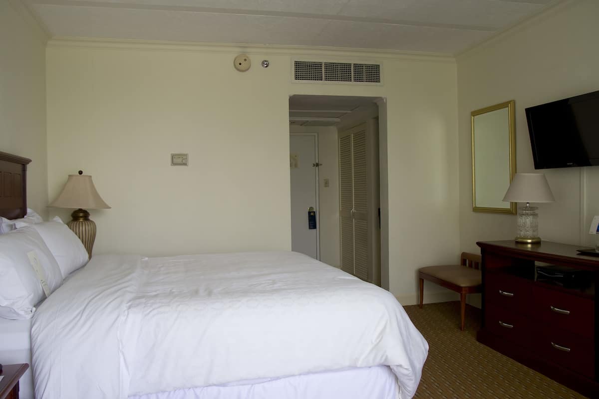 A hotel room with a large bed, a desk with a lamp, a chair, a television, and a mirror.