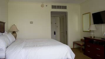 A hotel room with a large bed, a desk with a lamp, a chair, a television, and a mirror.