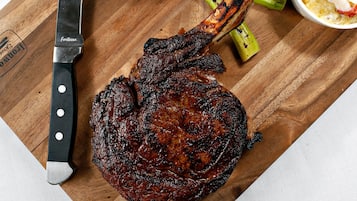 Una tabla de madera con un bistec a la parrilla, espárragos, un limón asado y una botella de vino tinto.