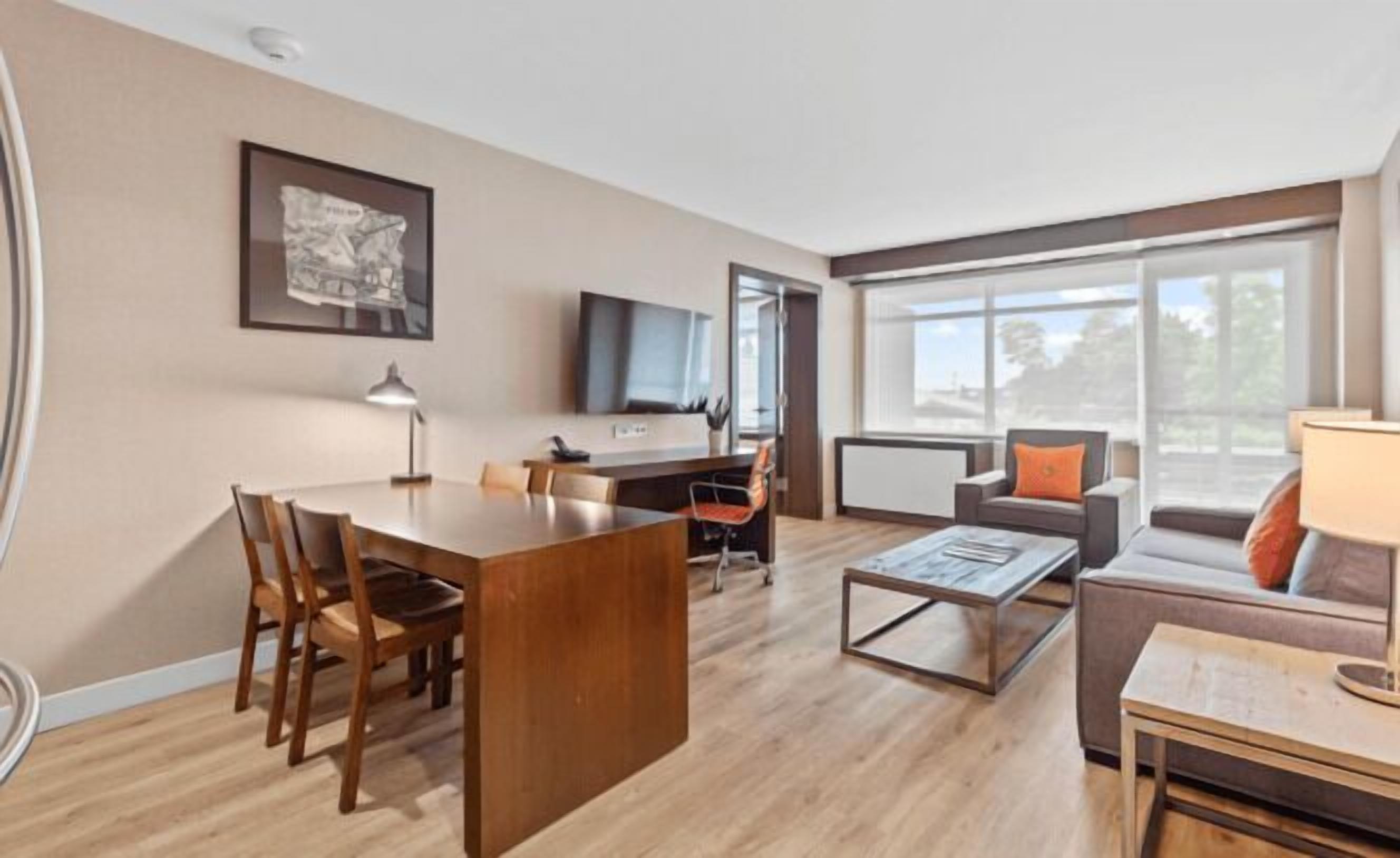 A modern living room with a wooden dining table, a sofa, a coffee table, and a TV mounted on the wall.