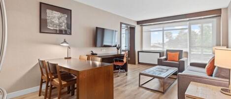 A modern living room with a wooden dining table, a sofa, a coffee table, and a TV mounted on the wall.