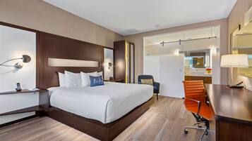 Habitación de hotel moderna con una cama grande, un escritorio, una silla y un baño visible a través de una puerta abierta.