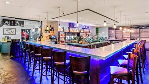 A bar area with a long counter, multiple stools, and a variety of bottles and glasses on shelves. - J House Greenwich (Riverside)