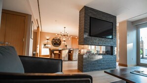 A modern living room with a fireplace, a dining area, and a kitchen in the background. - J House Greenwich (Riverside)