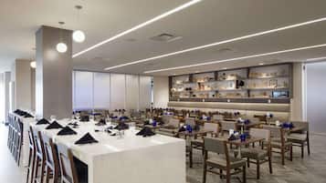 A modern dining area with long tables, chairs, and a central bar area.