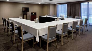 Un salón de conferencias con una larga mesa, sillas, un atril y una televisión.
