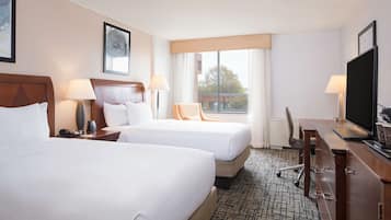 Une chambre d’hôtel avec deux lits, un bureau, une chaise, une télévision et une fenêtre donnant sur des immeubles.