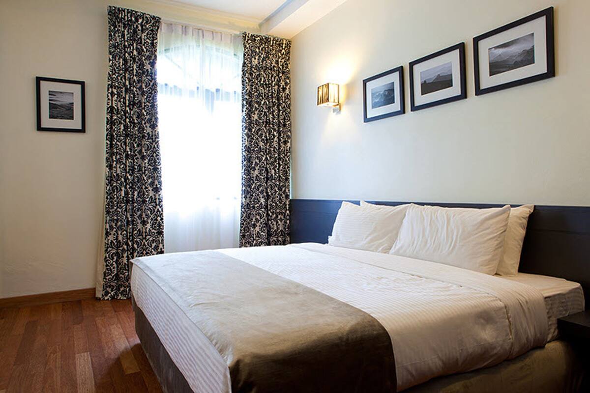 A hotel room with a large bed, a nightstand, a wall-mounted lamp, and three framed pictures on the wall.