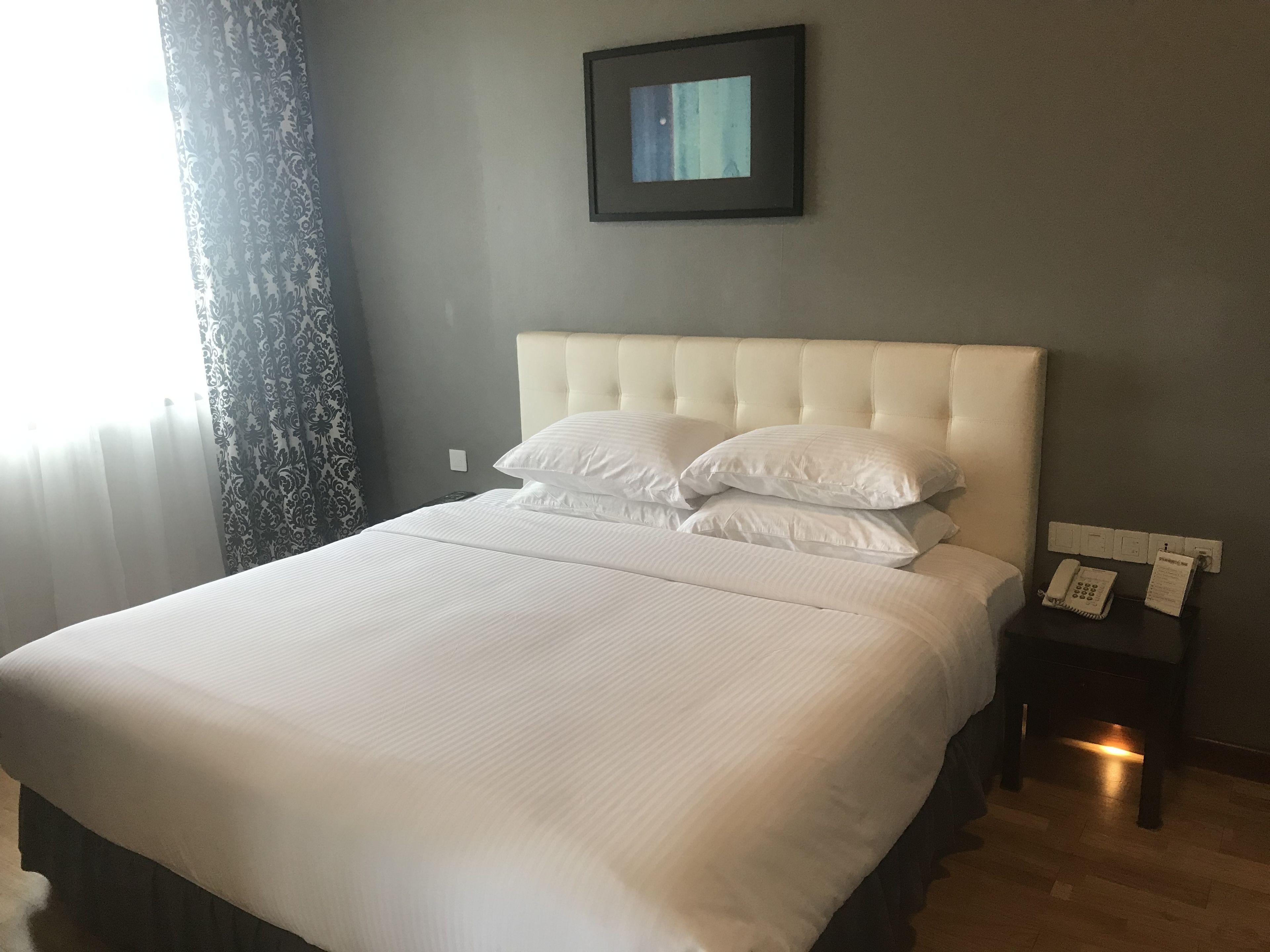 A neatly made bed with white linens and a tufted headboard, a bedside table with a lamp, and a framed picture on the wall.