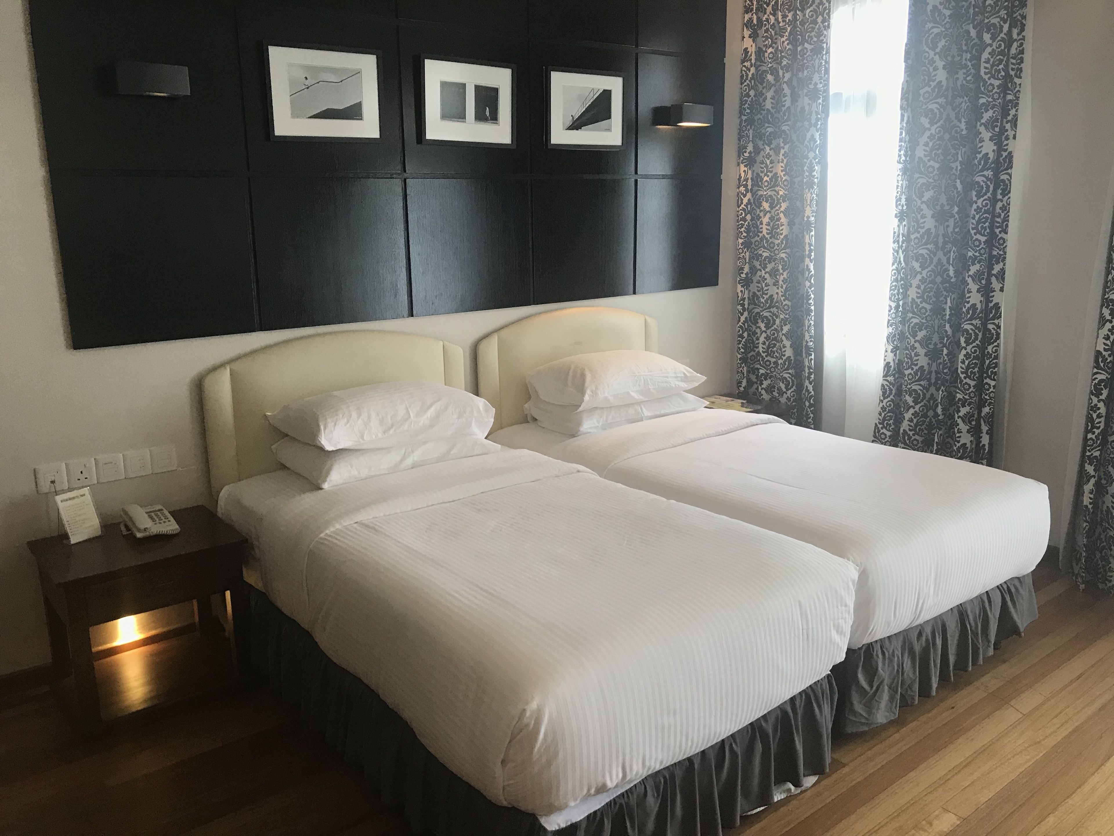 A double bed with two pillows, a bedside table with a phone and a notepad, and a wall with framed pictures.