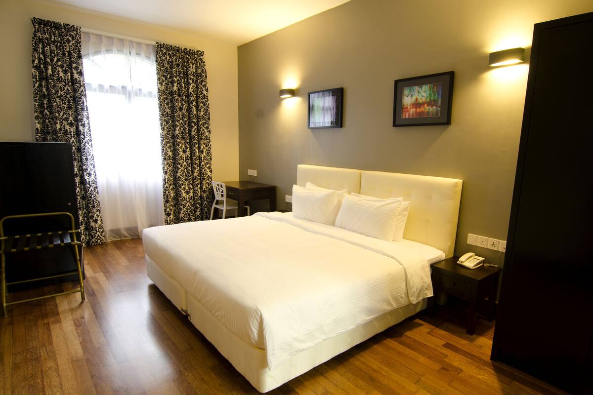 A hotel room with a large bed, bedside tables, a desk, a chair, a TV, and a wardrobe.