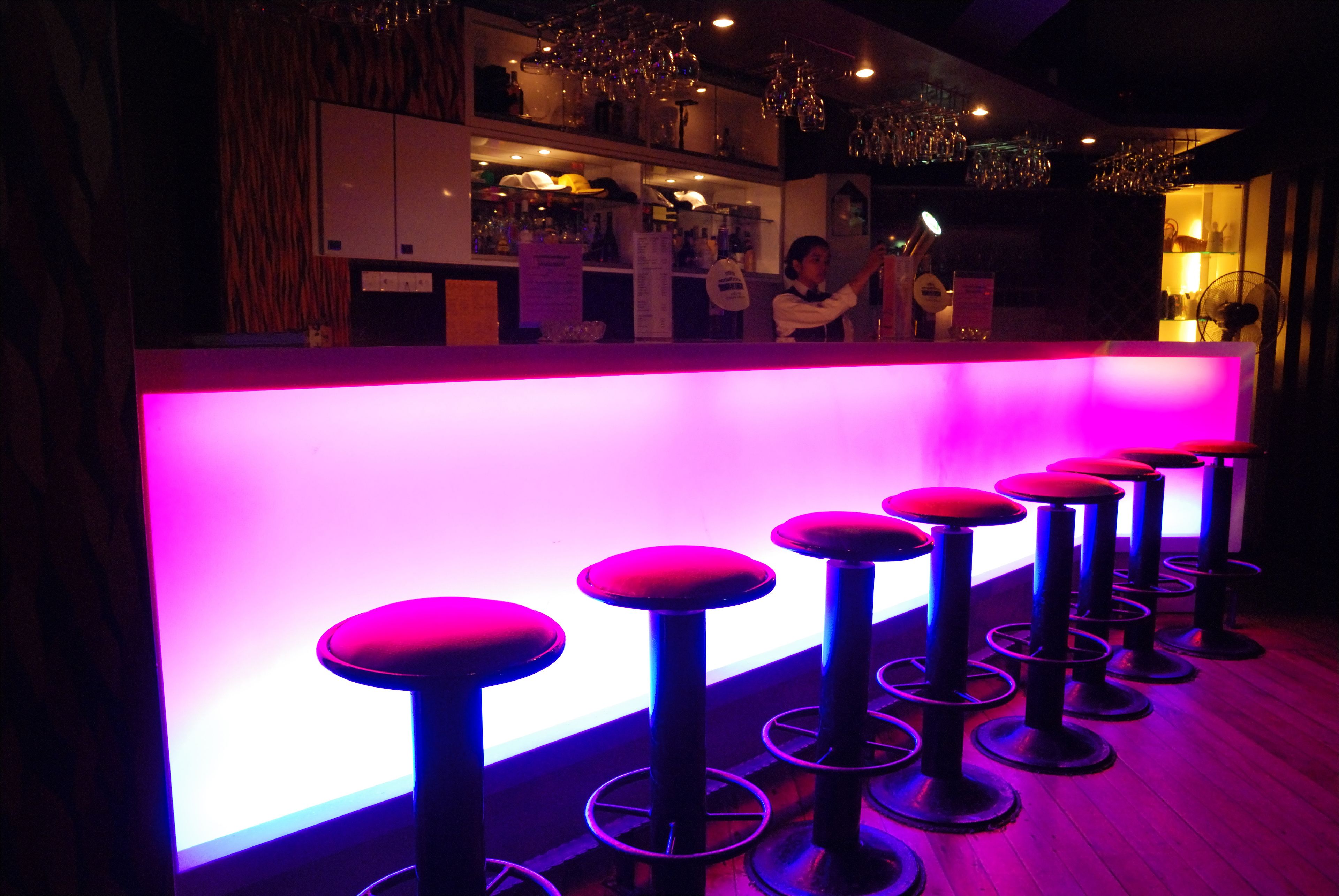 A bar area with a neon-lit bar counter and multiple stools.