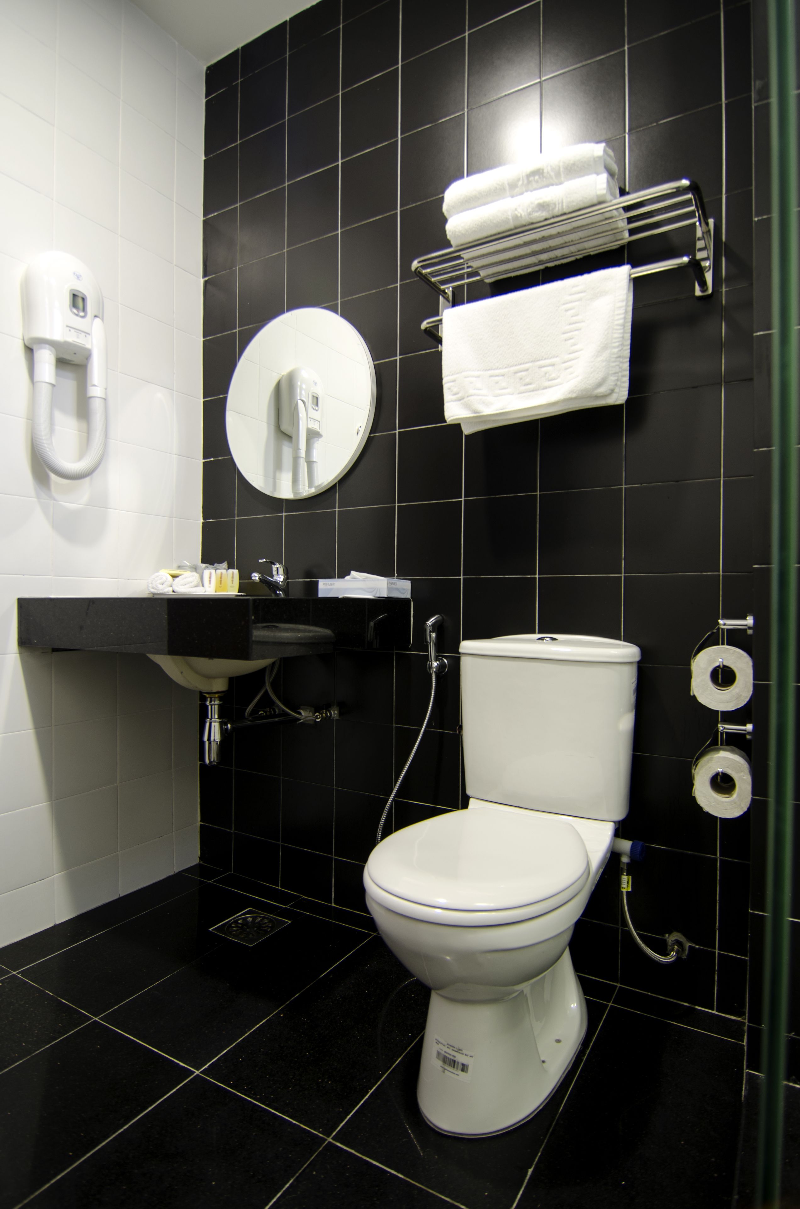 A modern bathroom with a white toilet, black tiled walls, a sink with a mirror, and a towel rack.