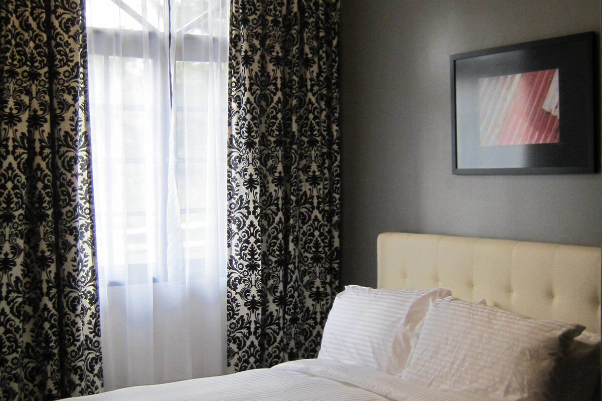 A hotel room with a bed, curtains, a ceiling light, and a framed picture on the wall.
