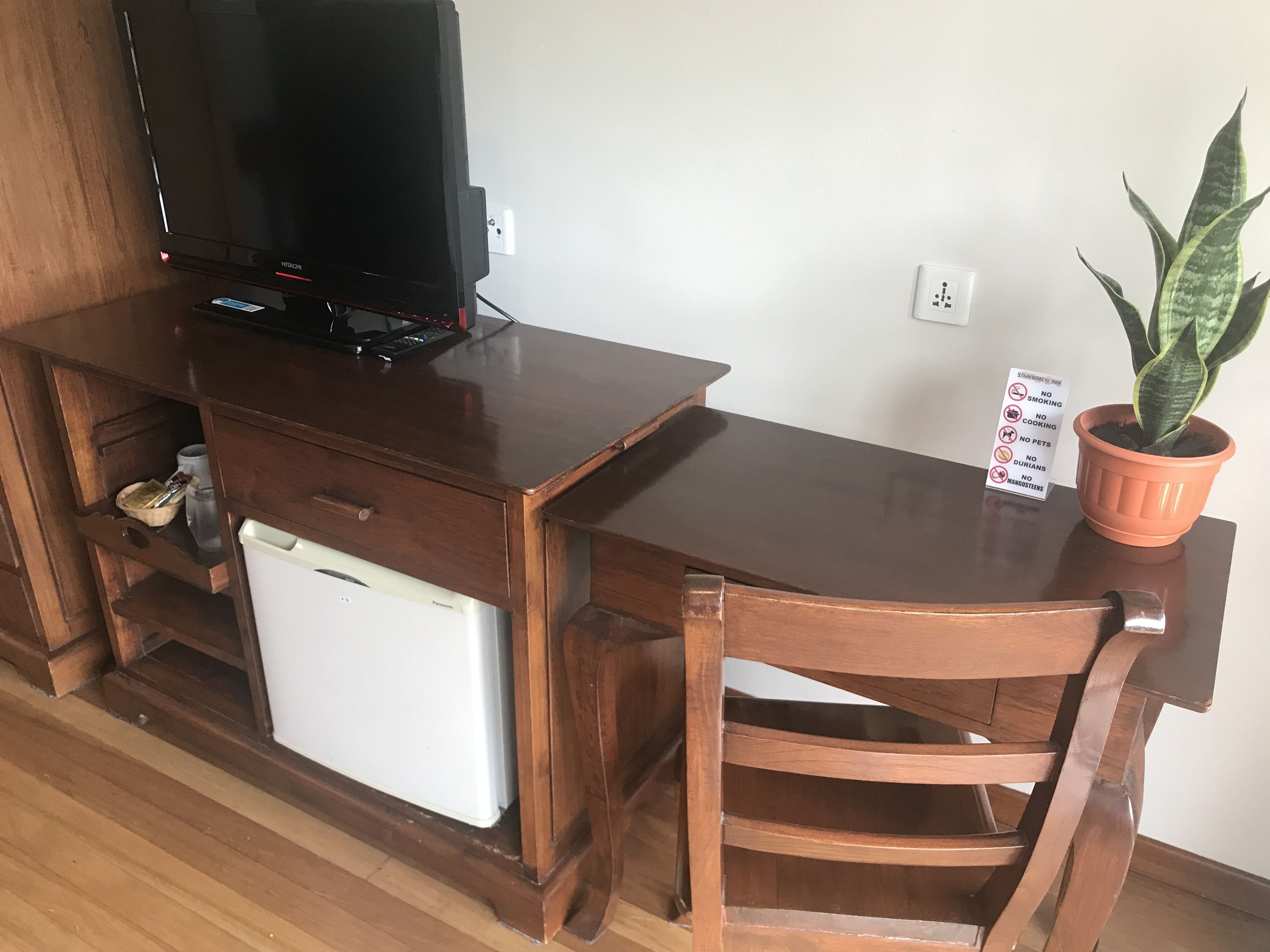 A wooden desk with a television, a small refrigerator, and a potted plant.