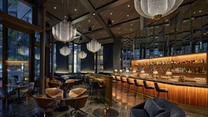 A modern bar area with high ceilings, large windows, and a variety of seating options including bar stools and cushioned chairs.