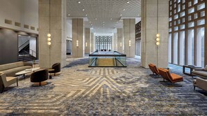 A spacious lobby with a central staircase, seating areas, and large windows.