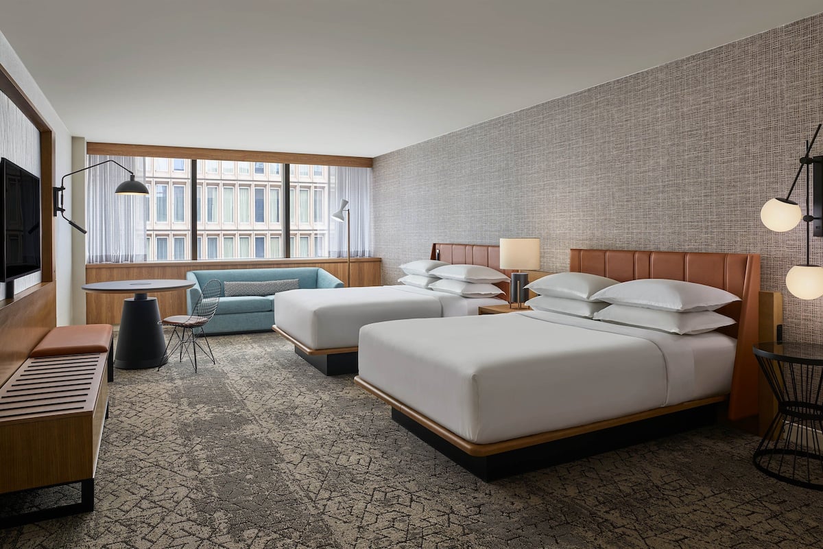 A hotel room with two beds, a sofa, a desk, and a large window with curtains.