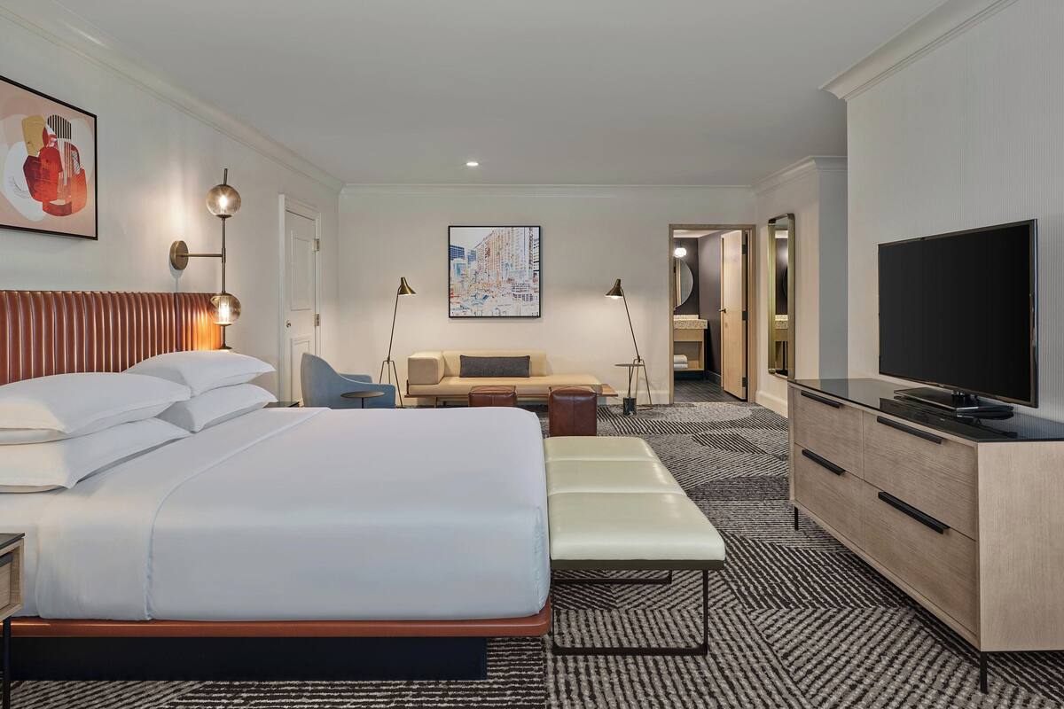 A hotel room with a large bed, a sofa, a TV, and a desk.