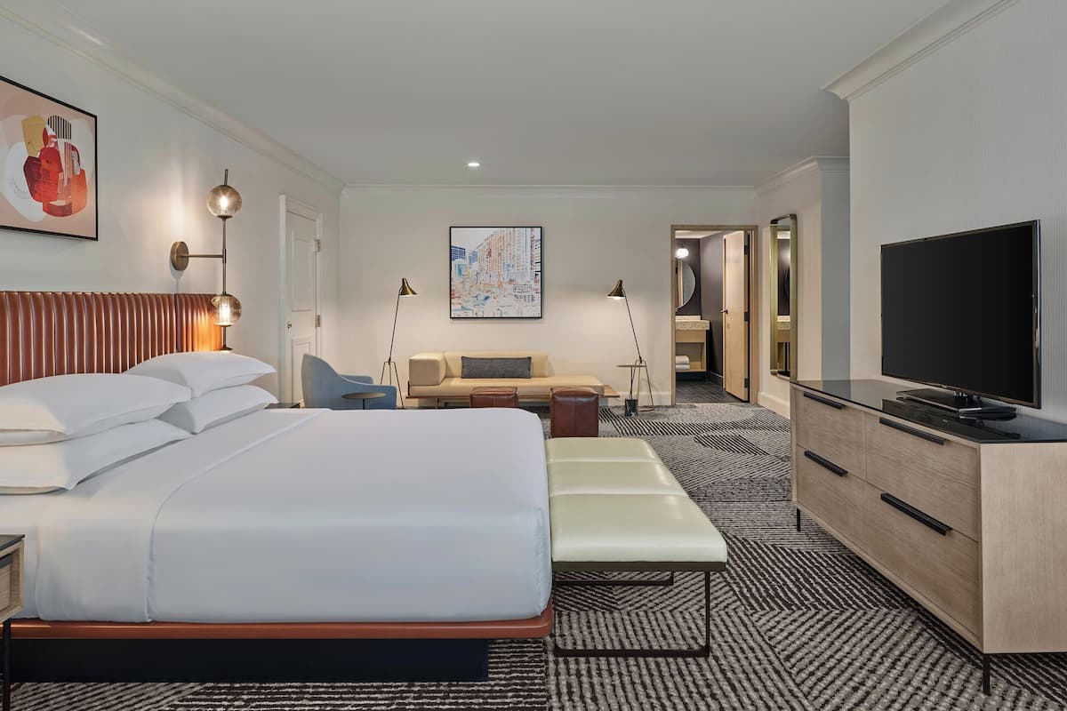 A hotel room with a large bed, a sofa, a TV, and a desk.