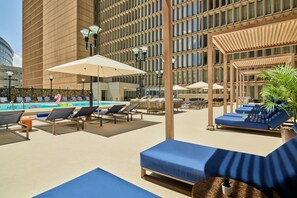 A rooftop pool area with lounge chairs, umbrellas, and a view of a modern building. - Sheraton Denver Downtown Hotel (Denver)