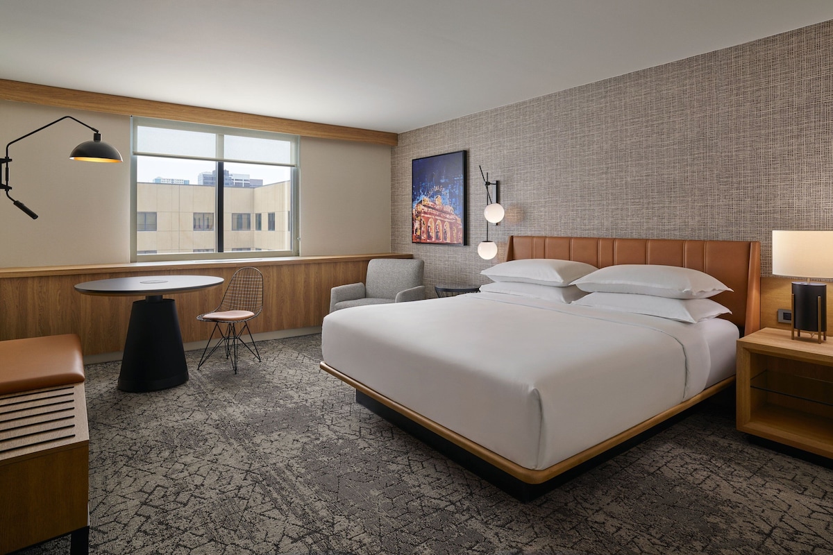 Ein Hotelzimmer mit einem großen Bett, einem runden Tisch, einem Stuhl, einem Schreibtisch und einer Lampe.