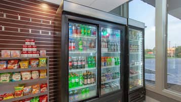 A vending machine stocked with snacks and beverages, located in a room with a brick wall and a window.