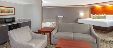 A hotel room with a bed, two armchairs, a small table, a sink, and a microwave.