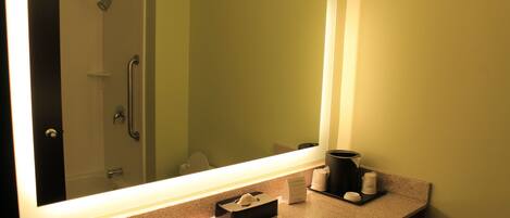 A bathroom with a large mirror, a sink, a towel dispenser, a soap dispenser, and a toilet paper holder.