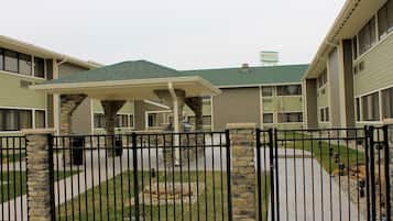 A gated courtyard with a covered seating area, stone pillars, and a pathway leading to a building with a green roof.