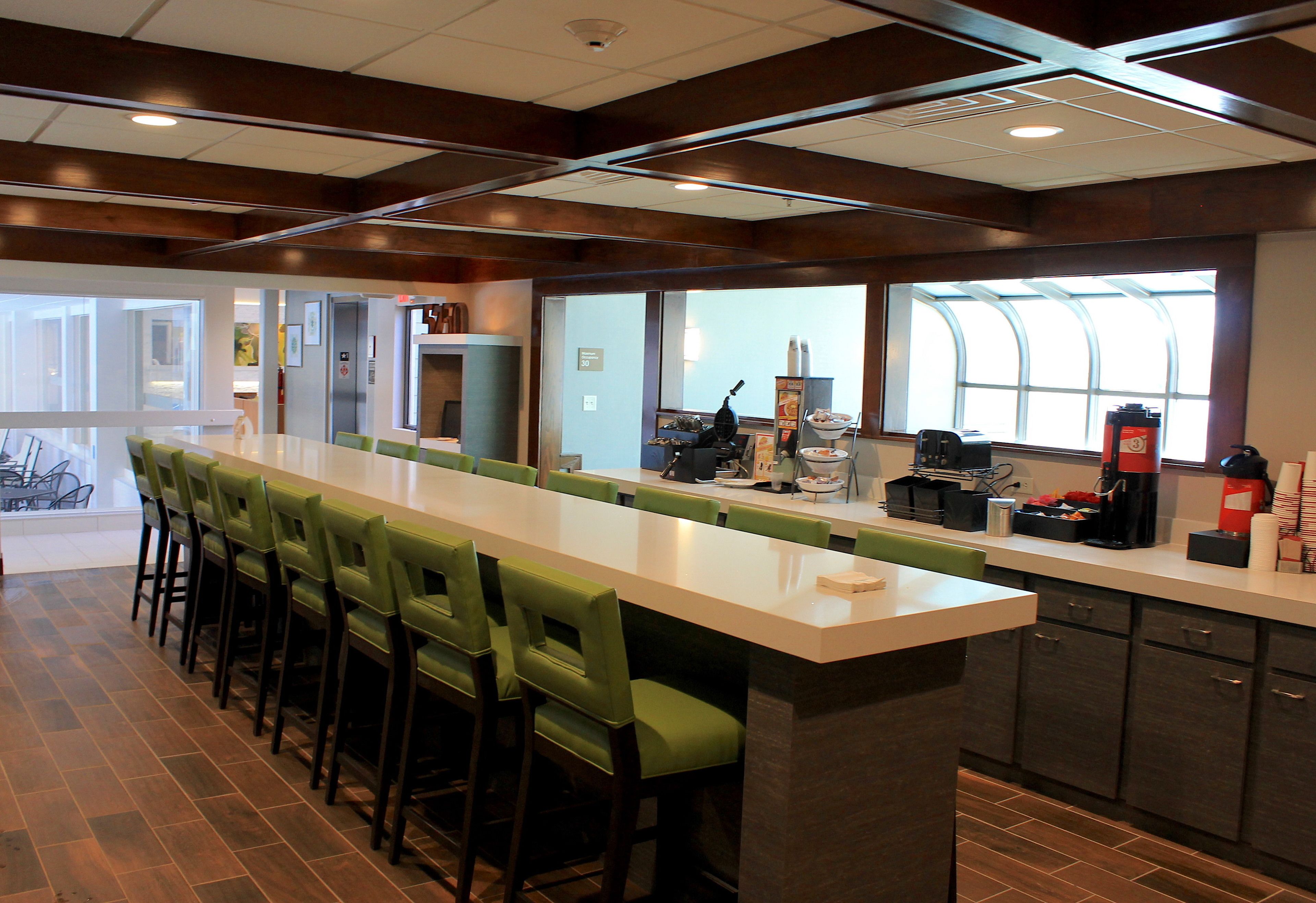 A modern kitchen area with a long counter, green bar stools, and a coffee station.