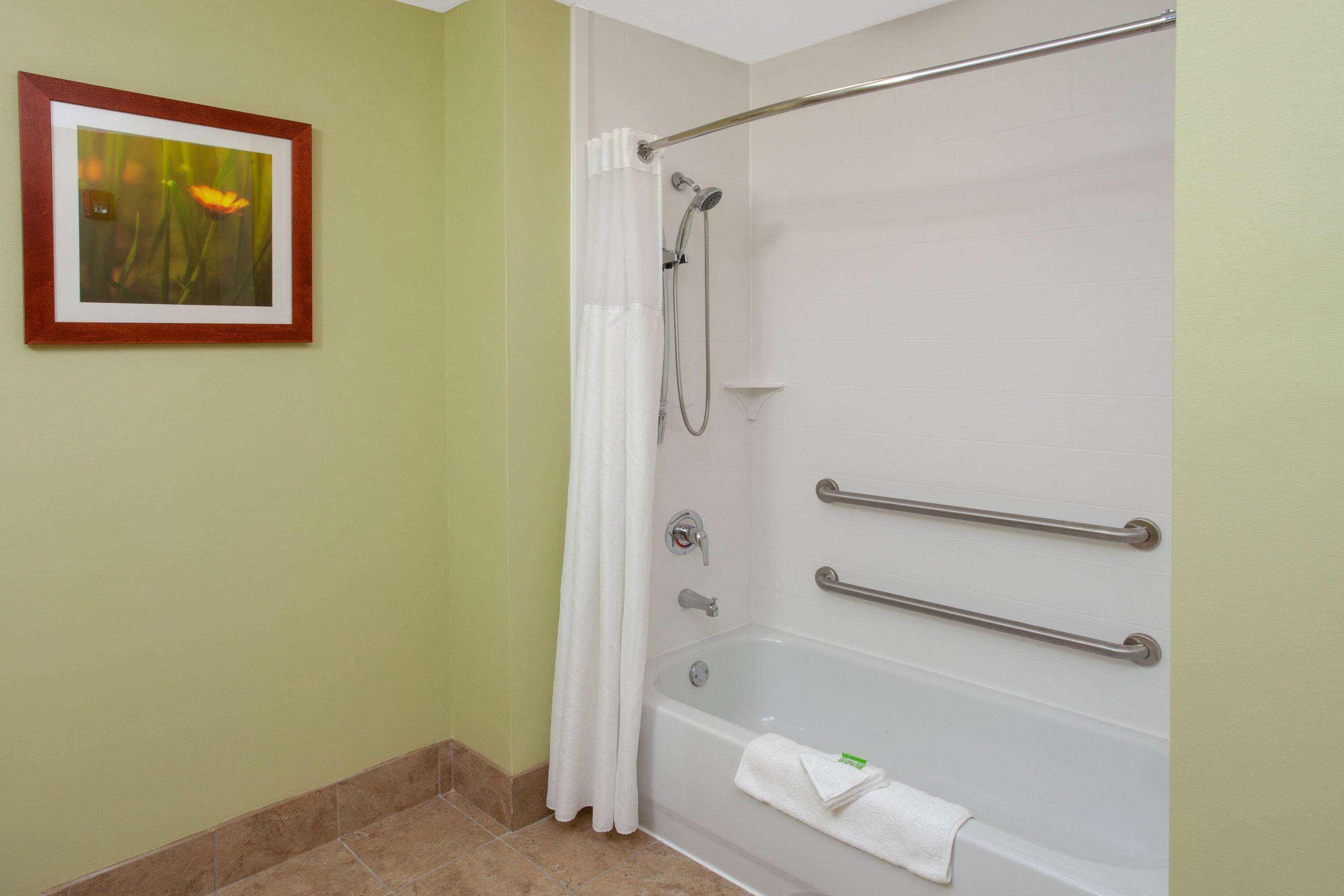 A bathroom with a bathtub, a shower, and a handrail.