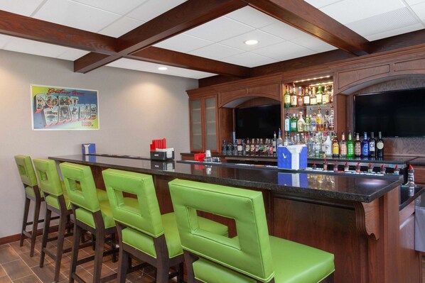 Una zona de bar con una barra alargada, taburetes verdes y una variedad de botellas de licor.