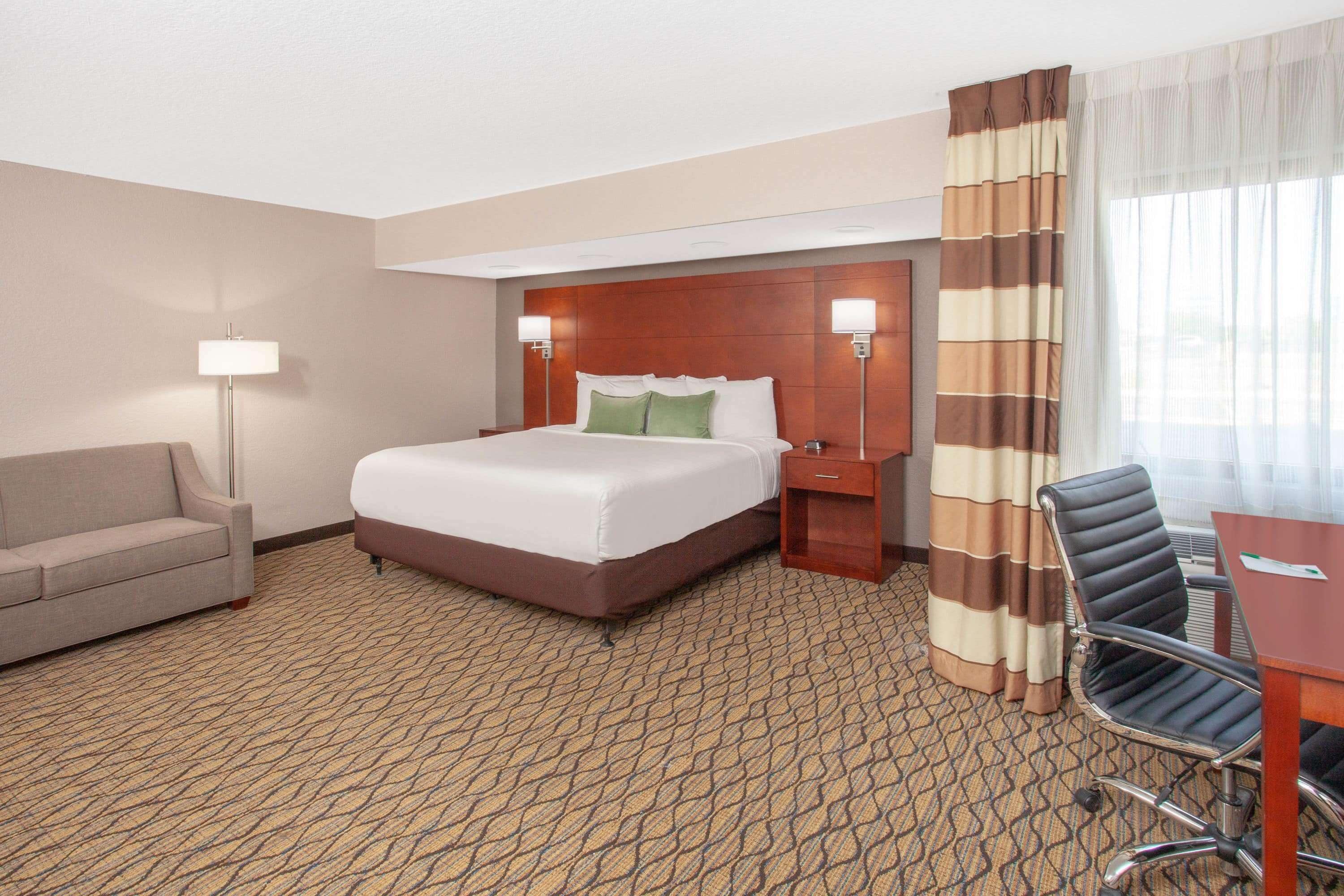 A hotel room with a large bed, a desk, a chair, a sofa, and a lamp.