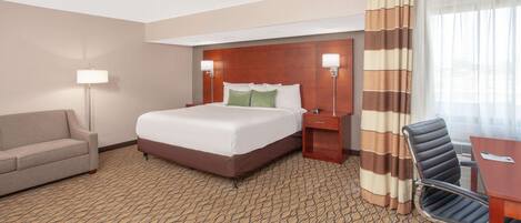 A hotel room with a large bed, a desk, a chair, a sofa, and a lamp.
