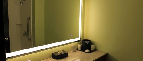 A bathroom with a large mirror, a sink, a toilet, and a shower.