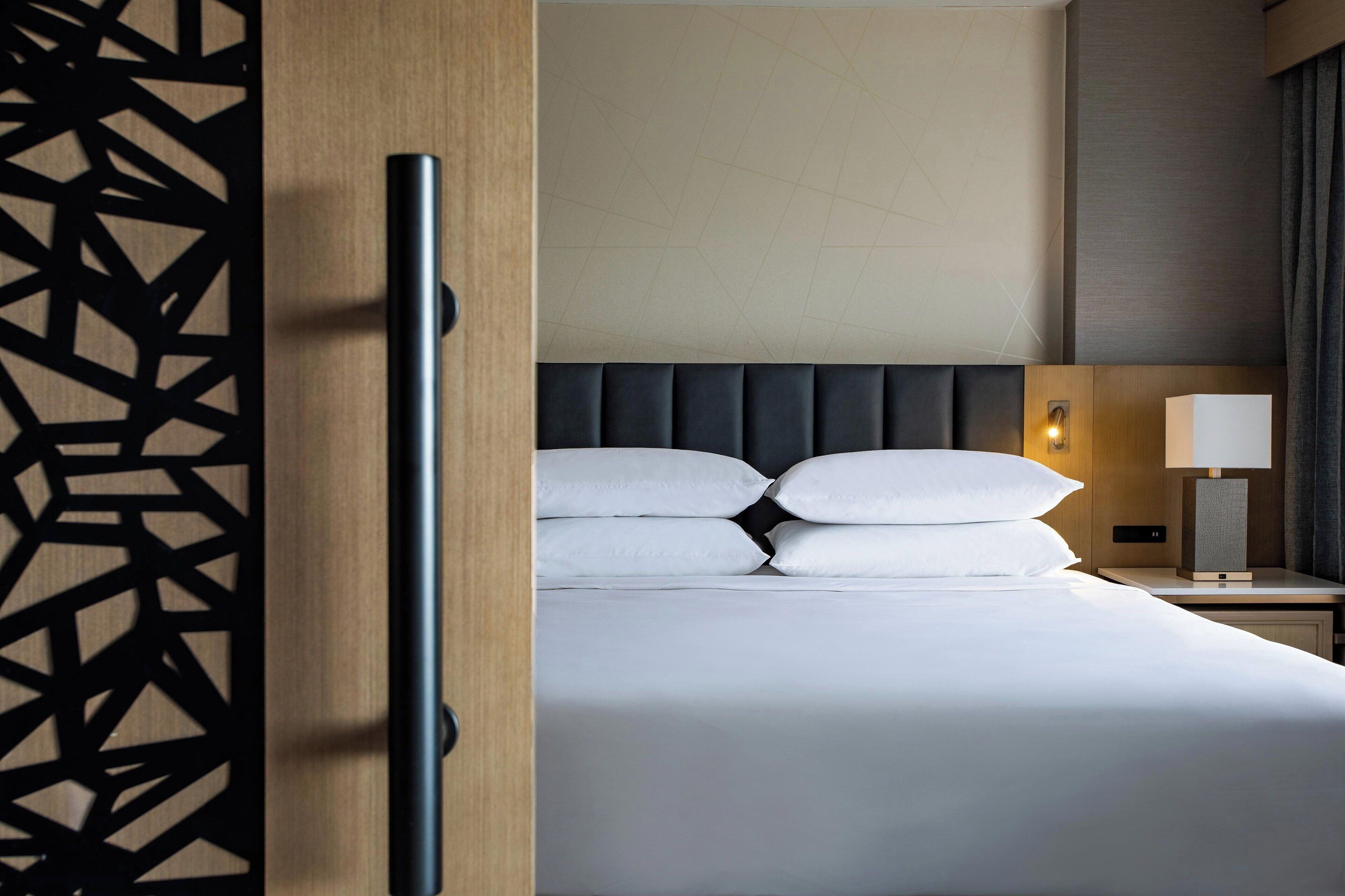 Une chambre d’hôtel comprenant un lit, une table de chevet, une lampe et un panneau décoratif.